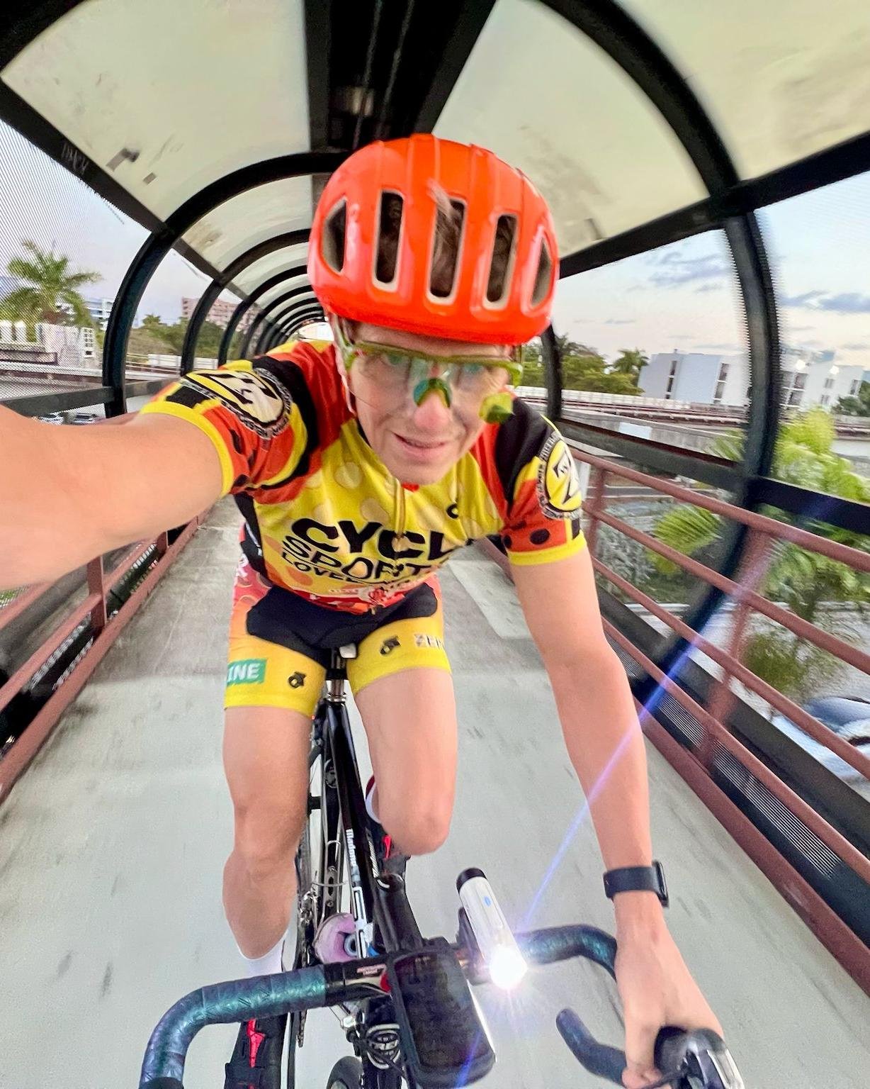 Jay Miller, co-founder of Middle Ground Cycling, rides through a covered bridge in Girona wearing safety gear—demonstrating the blend of adventure and urban cycling routes.
