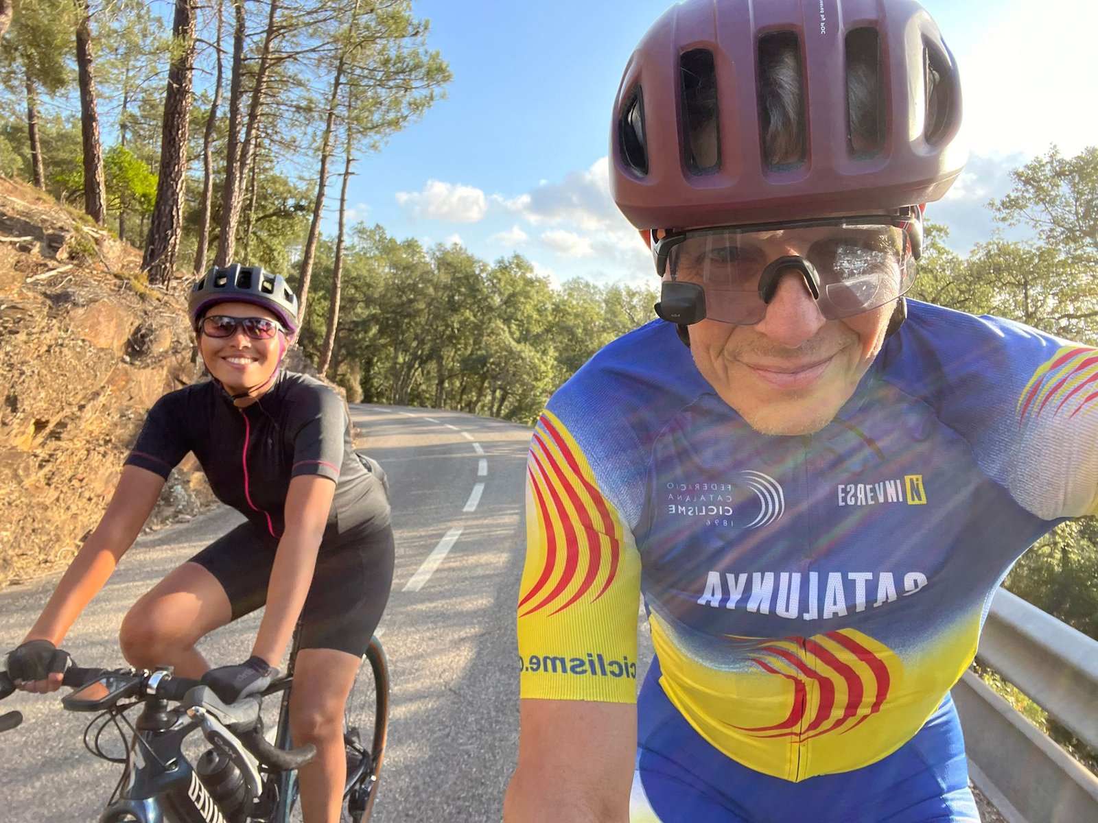 Jay and Daylin Miller, founders of Middle Ground Cycling, smiling while riding through Girona’s scenic forest roads—highlighting their passion for personalized cycling tours in Catalonia.